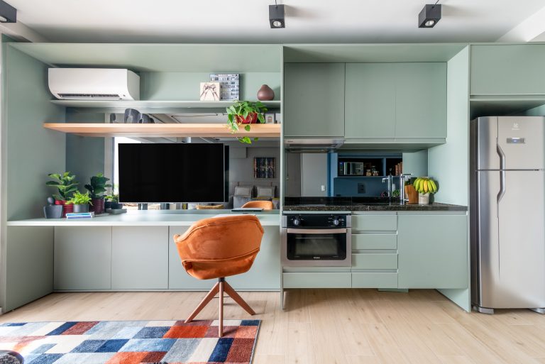 Caixa de marcenaria verde abriga cozinha, bancada e tv em estúdio de 34 m²